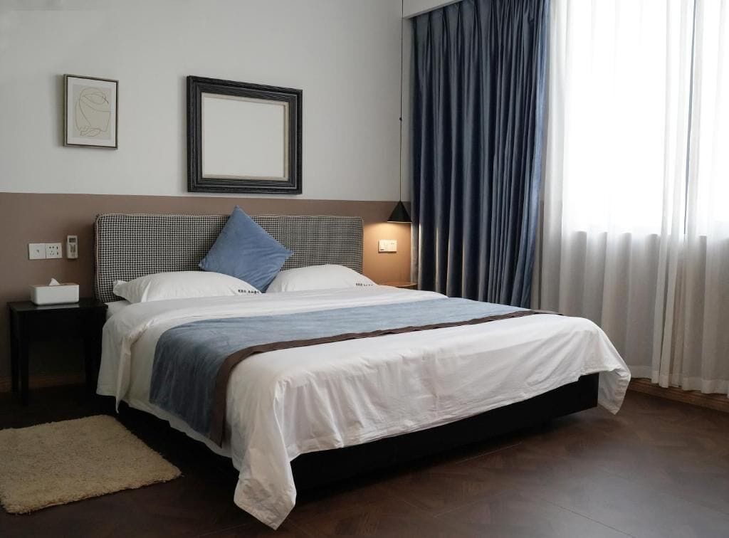 Una cama bien hecha con una colcha blanca y azul, un cabecero a cuadros y una lámpara de noche.