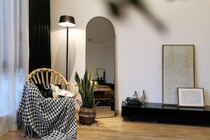 Uma sala de estar moderna com uma poltrona estampada em xadrez, um abajur, um vaso de planta, um espelho e um documento emoldurado numa prateleira.