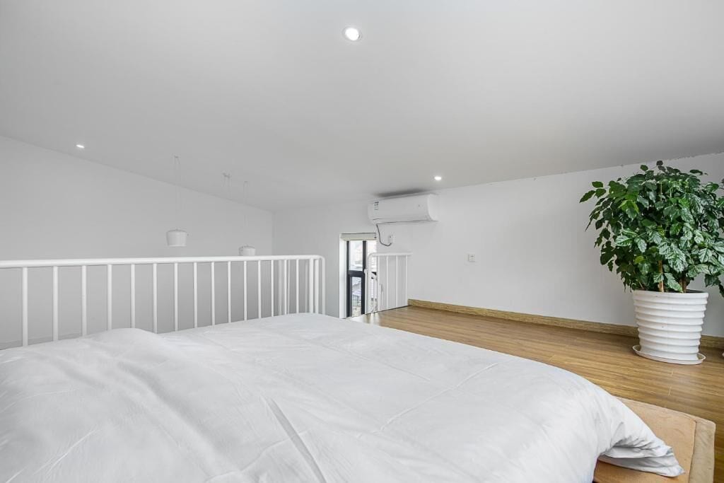 Une chambre à coucher avec un lit, des murs blancs, un ventilateur de plafond, un appareil de climatisation et une plante en pot.