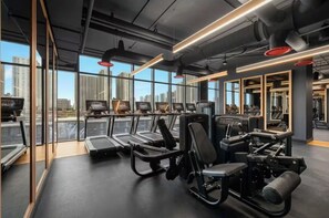 Ein modernes Fitnessstudio mit Laufbändern, Kraftgeräten und großen Fenstern mit Blick auf die Stadt.
