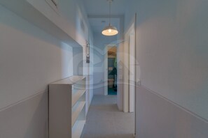 A narrow hallway with white walls, a ceiling light, and a door leading to a bathroom.