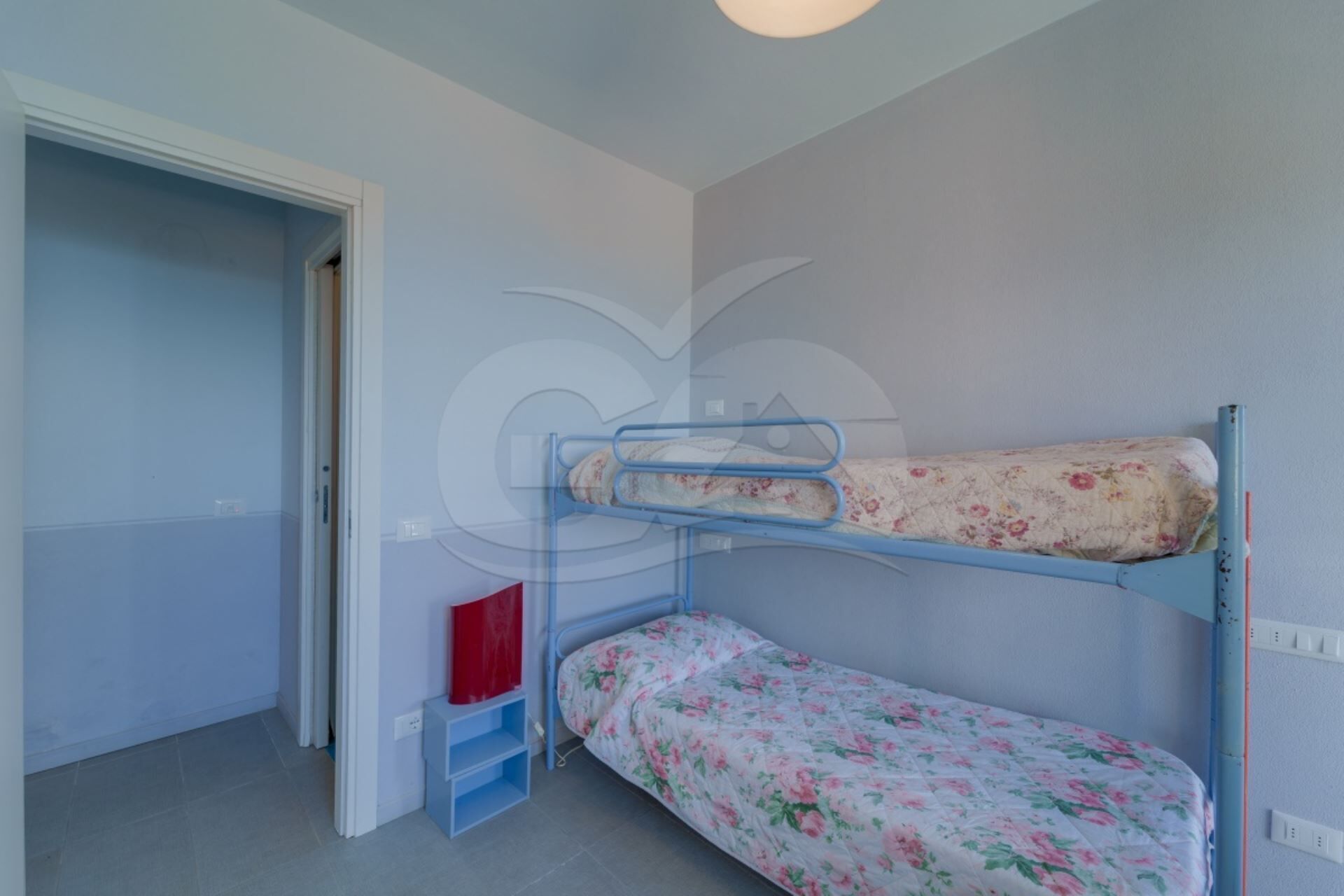 A room with a bunk bed, a small desk, and a door leading to another room.