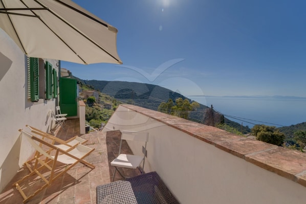 Una terraza con vistas al mar, una silla, una mesa y una sombrilla.