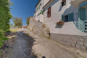 Un estrecho sendero de piedra que conduce a un edificio blanco con contraventanas verdes y un muro de piedra.