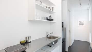 Una cocina moderna con placa de inducción integrada, pileta de acero inoxidable y muebles color blanco.