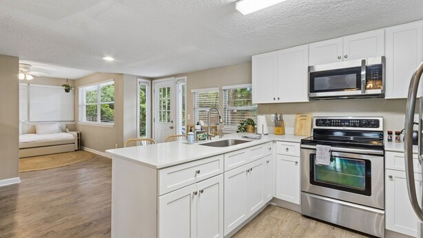 A modern kitchen with white cabinets, stainless steel appliances, and a large island. - Blake's Place: Quiet 3bd/2ba home with Mega Hot Tub + Cold Plunge (Jacksonville Beach)