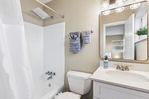 Een badkamer met douche, toilet, wastafel en een spiegel met verlichting.