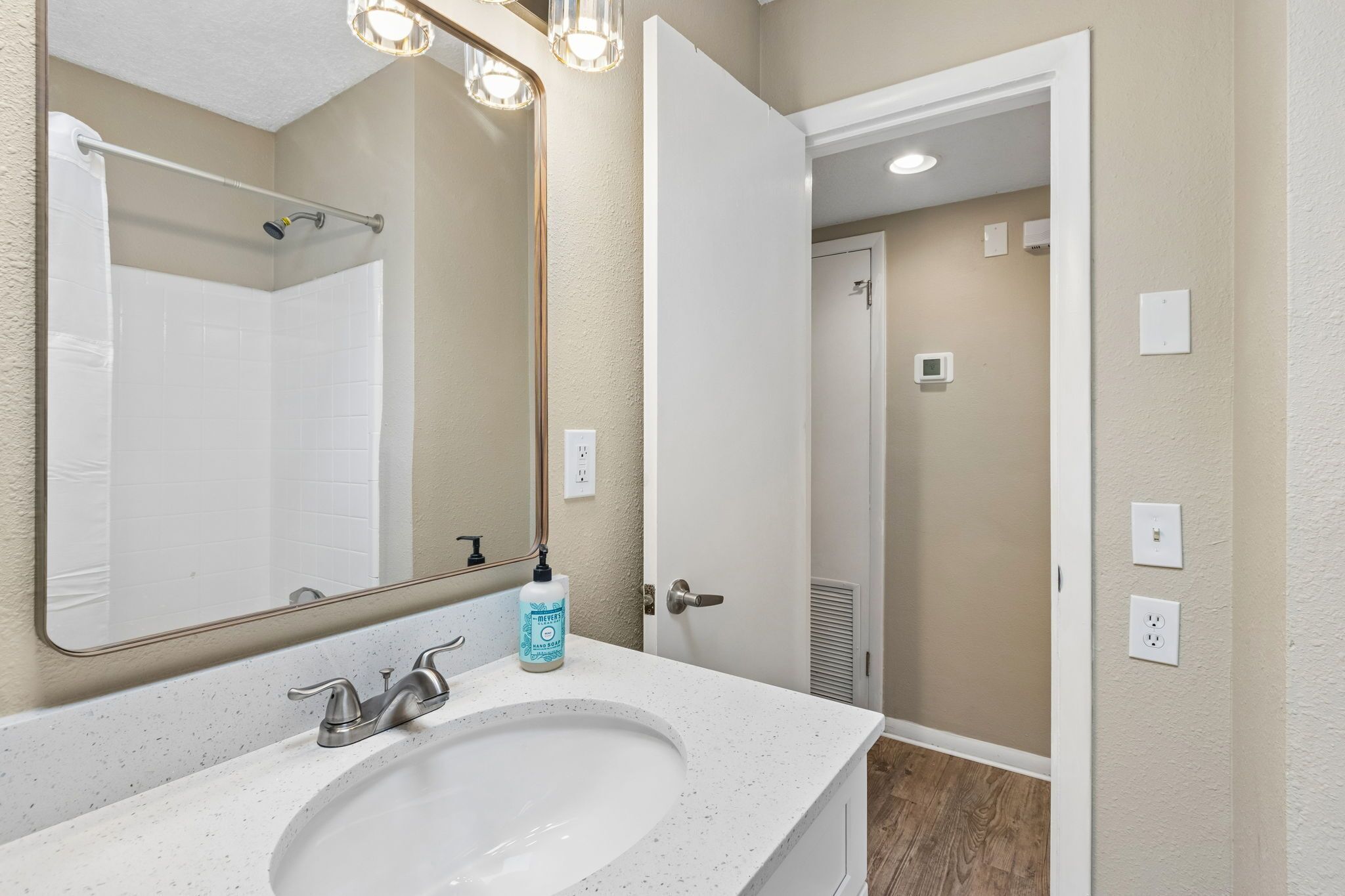 A bathroom with a white sink, a mirror, a shower curtain rod, and a door leading to another room.