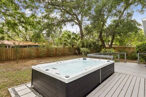 Een hottub op een houten terras, met een houten omheining en bomen op de achtergrond.
