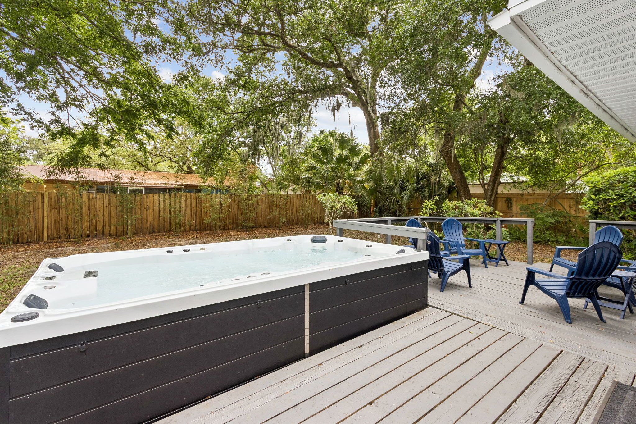 Un bain à remous sur une terrasse en bois, avec des chaises, le tout entouré d’arbres.