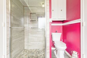 Ein Badezimmer mit Dusche, Toilette und einer rosa Wand.