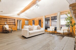 Een ruime woonkamer met een witte bank, twee fauteuils, houten kasten en een groot raam.