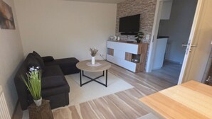 A modern living room with a sectional sofa, a small round table, and a flat-screen TV mounted on a stone wall. - "Auszeit" Vacation Rental in Irslingen  (Dietingen)