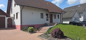 A two-story house with a red-tiled roof, a number '5' on the wall, and a car parked in the driveway.