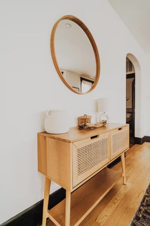 Ein Konsolentisch aus Holz mit einem Spiegel, einer weißen Krug und einem Korbwäschekorb vor einer weißen Wand.