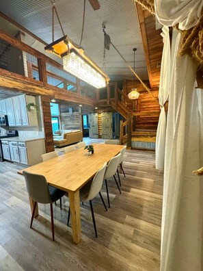 Tilava ruokailutila, jossa on puinen pöytä ja tuolit, taustalla keittiö ja portaat, jotka johtavat ylemmälle tasolle.