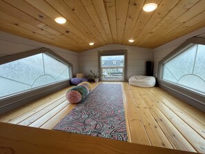 Ein Schlafzimmer im Loft-Stil mit Holzboden, einem gemusterten Teppich, einem Sitzsack und Blick durch ein großes Fenster.