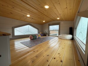 Una habitación con piso de madera, un ventanal grande, un techo con vigas de madera y una colchoneta de yoga.