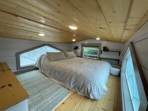 Ein Schlafzimmer mit Bett, Fenster, Nachttisch und Decke mit Holzbalken.