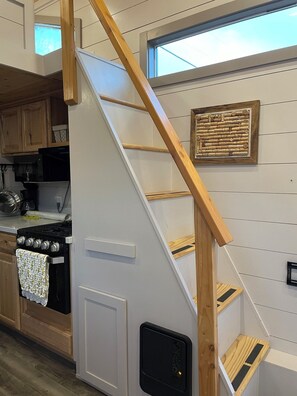 Una cocina con una escalera de madera, estufa, armarios y ventana.