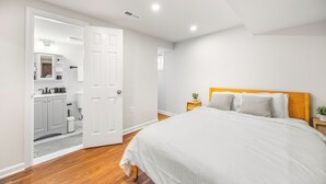 A bedroom with a bed, a nightstand, a wooden headboard, and a door leading to a bathroom.