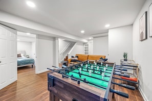 Una habitación con mesa de fútbol, cama, sofá y escalera.