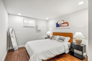 Una camera da letto con un letto, comodini, una lampada, uno specchio, una finestra e un'opera d'arte appesa al muro.