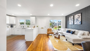 A modern kitchen with white cabinets, a central island, and a dining area with a sofa and coffee table.