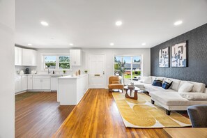 A modern kitchen with white cabinets, a central island, and a dining area with a sofa and coffee table.