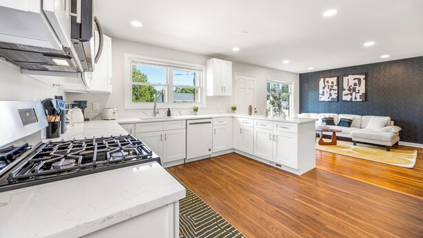 A modern kitchen with white cabinetry, a gas stove, and a dining area with a sofa and a rug.