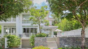 A modern two-story building with a white exterior, a covered entrance, and a stone wall. - Premier Villa Da Nang by DDH (Da Nang)