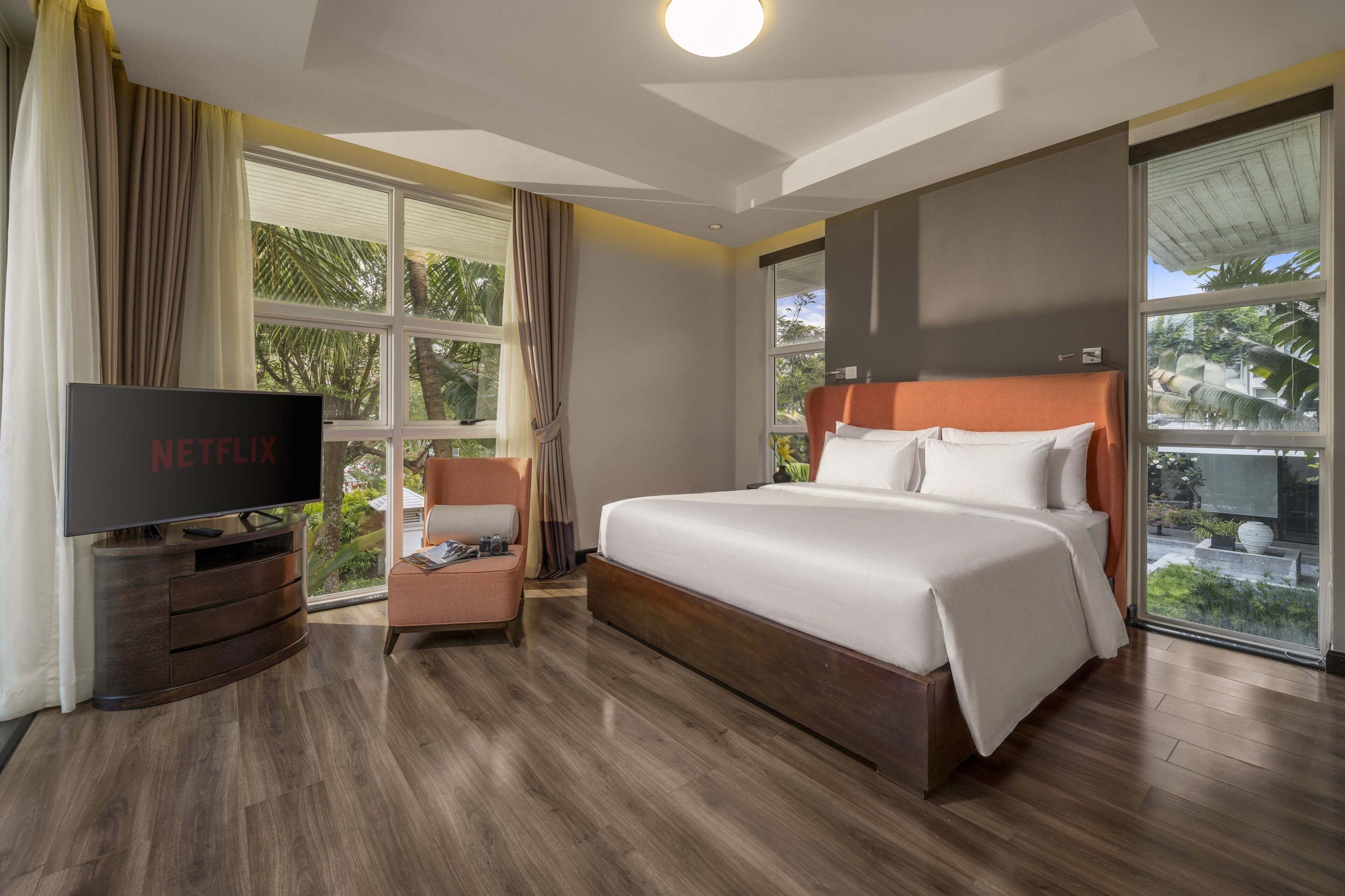 A hotel room with a large bed, a television, a chair, and a window with curtains.