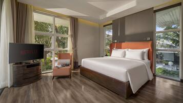 A hotel room with a large bed, a television, a chair, and a window with curtains.