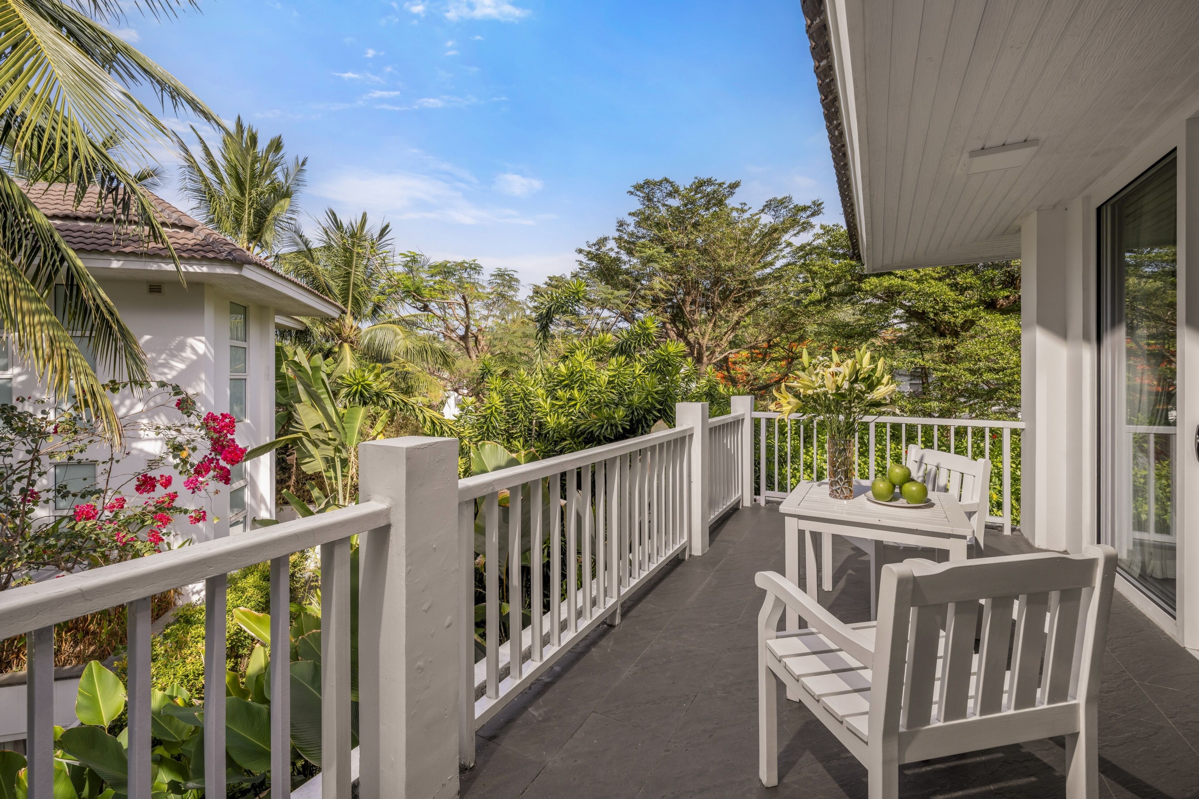 Ein Balkon mit weißen Geländern, einem Tisch und Stühlen, umgeben von üppiger Vegetation und verschiedenen Pflanzen.