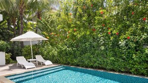A swimming pool with a tiled floor, surrounded by lush greenery and a white umbrella. - Premier Villa Da Nang by DDH (Da Nang)