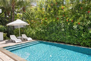 A swimming pool with a tiled floor, surrounded by lush greenery and a white umbrella. - Premier Village Da Nang by DDH (Da Nang)
