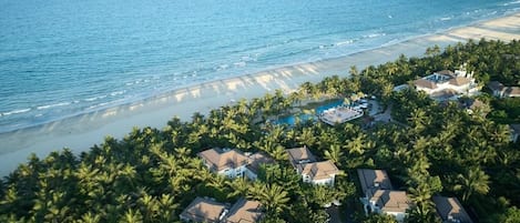 Vue aérienne d’un quartier résidentiel situé sur la côte, avec des maisons, une piscine et une plage.
