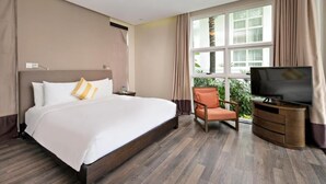A hotel room with a bed, a TV, a chair, and a window with curtains. - Premier Villa Da Nang by DDH (Da Nang)