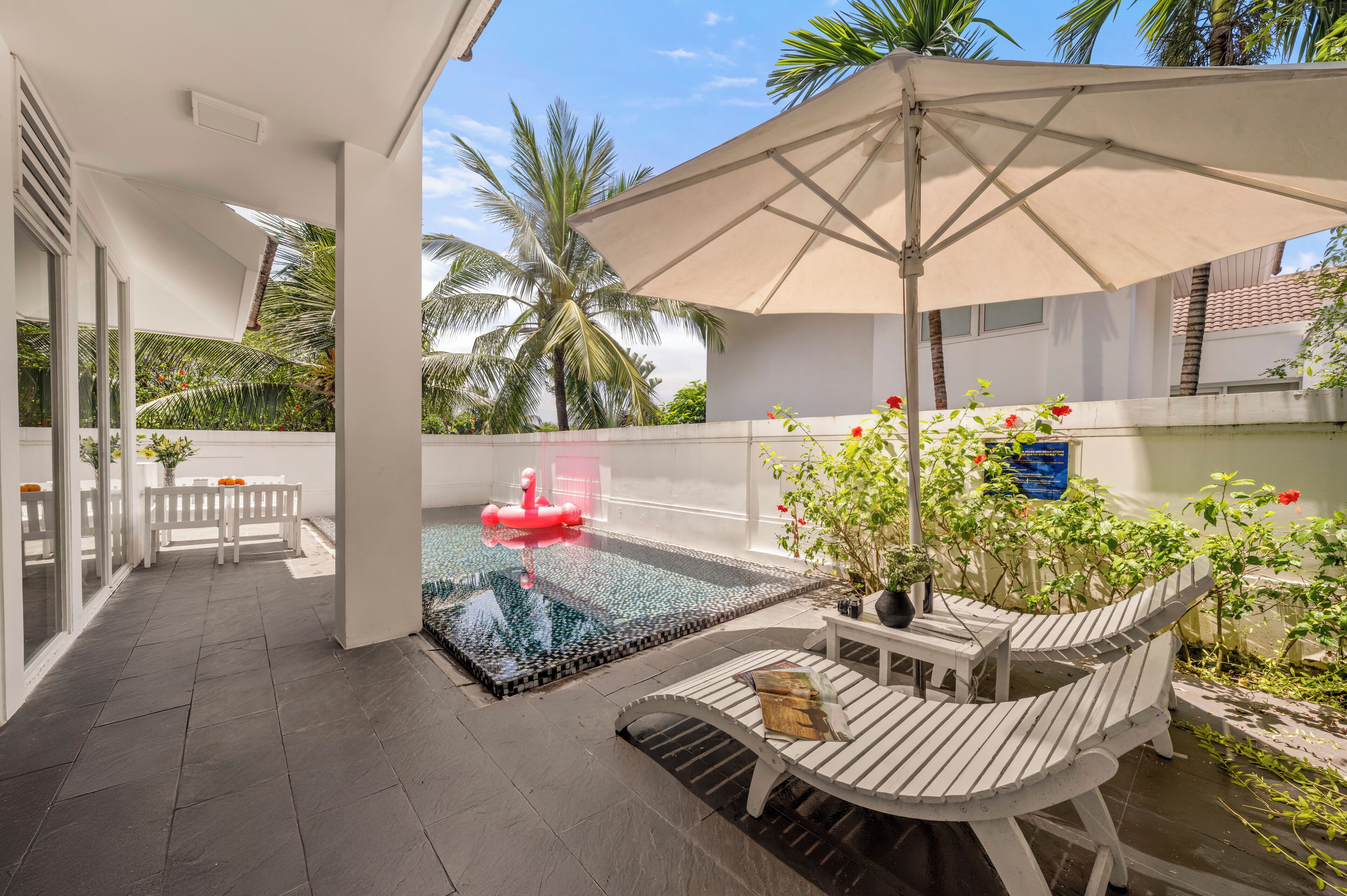 A rooftop pool area with a floating flamingo, a white chair, and a table with a magazine.