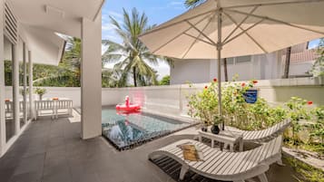 A rooftop pool area with a floating flamingo, a white chair, and a table with a magazine.