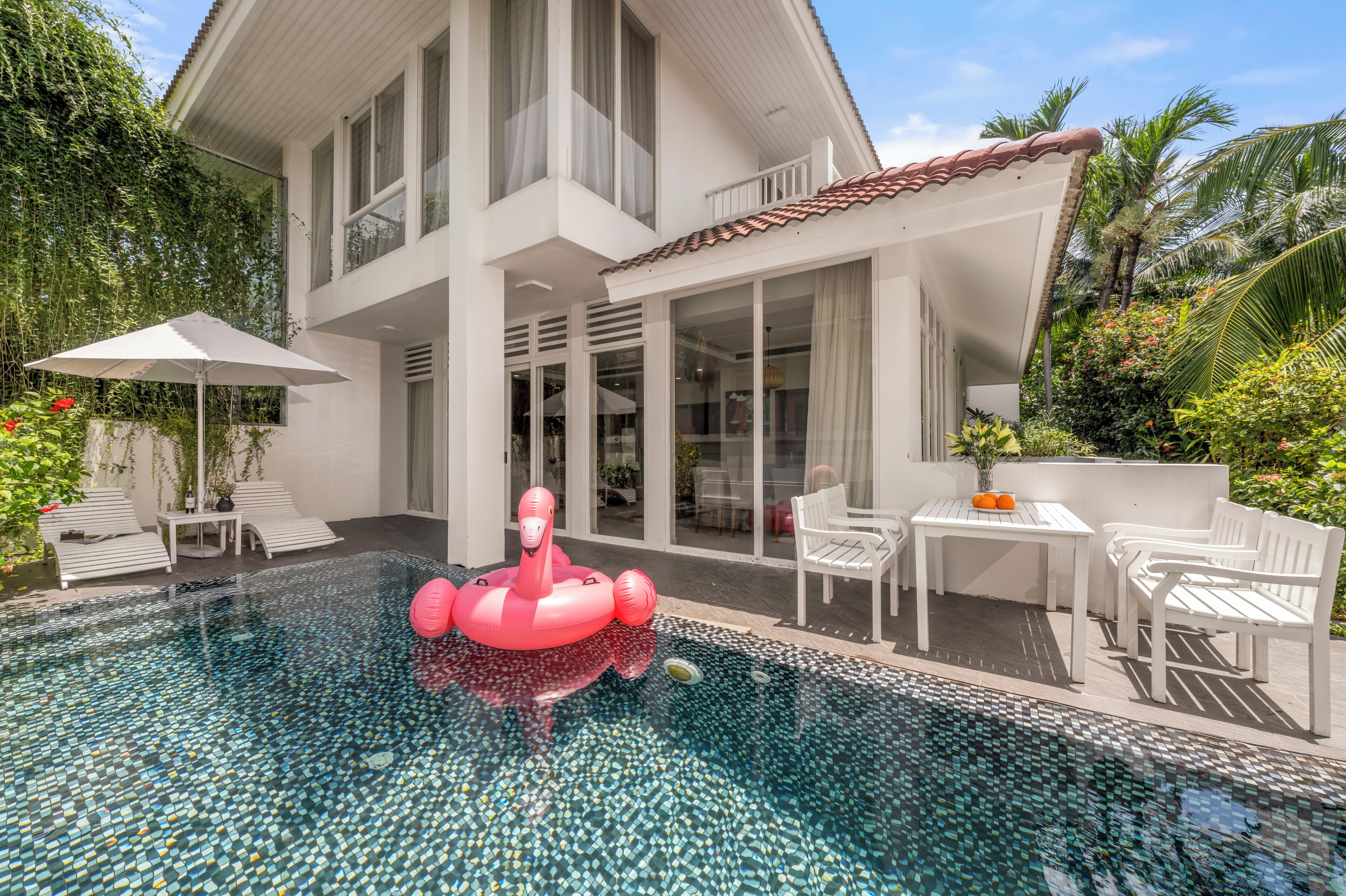 Une maison moderne dotée d’une piscine, de mobilier d’extérieur et d’un flotteur en forme de flamant rose.