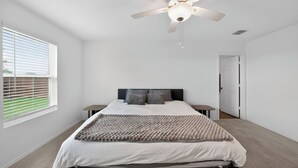Ein Schlafzimmer mit einem Bett, einem Deckenventilator, einem Fenster mit Jalousien und einer Tür.