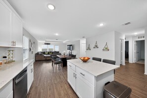 A modern kitchen with white cabinetry, a central island, and a dining area with a sofa and chairs. - Modern 4BR Retreat Near Fort Worth, Sleeps 5 (Crowley)