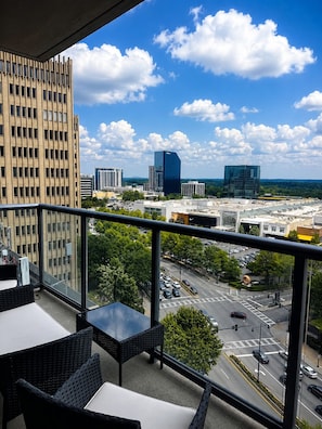 Un balcon aménagé avec du mobilier d’extérieur, offrant une vue sur le paysage urbain et les bâtiments modernes.