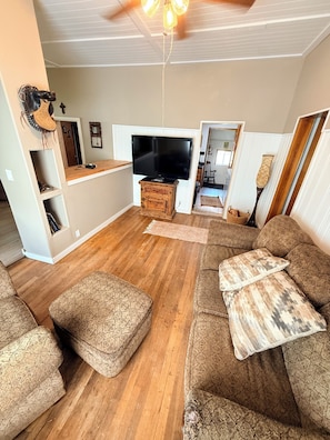 A living room with a large TV, wooden furniture, and a ceiling fan. - Cozy  2-bedroom house in beautiful Sundance Wyoming perfect for relaxing stays (Sundance)