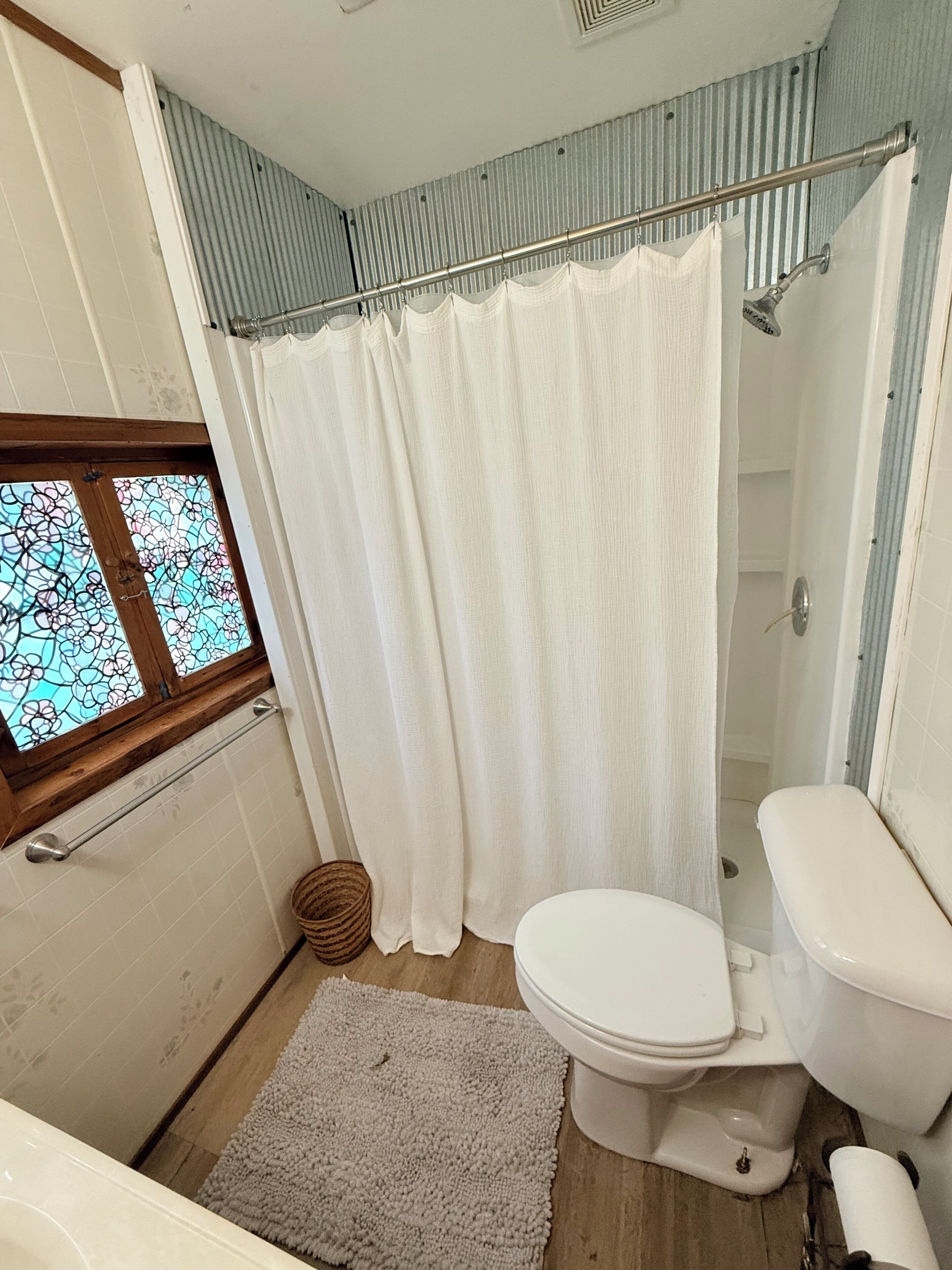 A bathroom with a shower, toilet, and a window with stained glass.