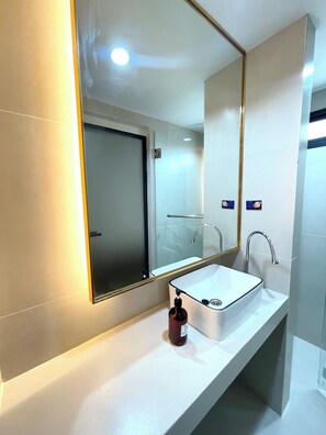 A modern bathroom with a large mirror, a white sink, and a handheld soap dispenser.