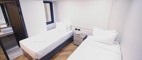 A hotel room with two beds, a small bedside table, a mirror, and an air conditioning unit.