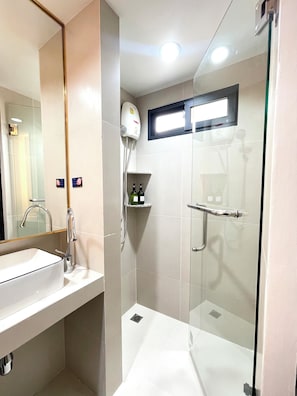 Een moderne badkamer met een glazen douchecabine, een witte wastafel en een handdouche.