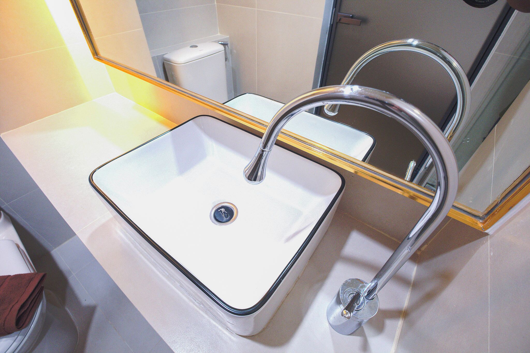 A bathroom with a white sink, chrome faucet, and a mirror with a gold frame.